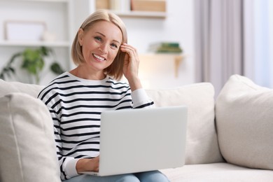 Happy middle aged woman using laptop on sofa at home