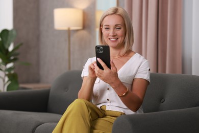 Photo of Portrait of smiling middle aged woman with smartphone on sofa at home