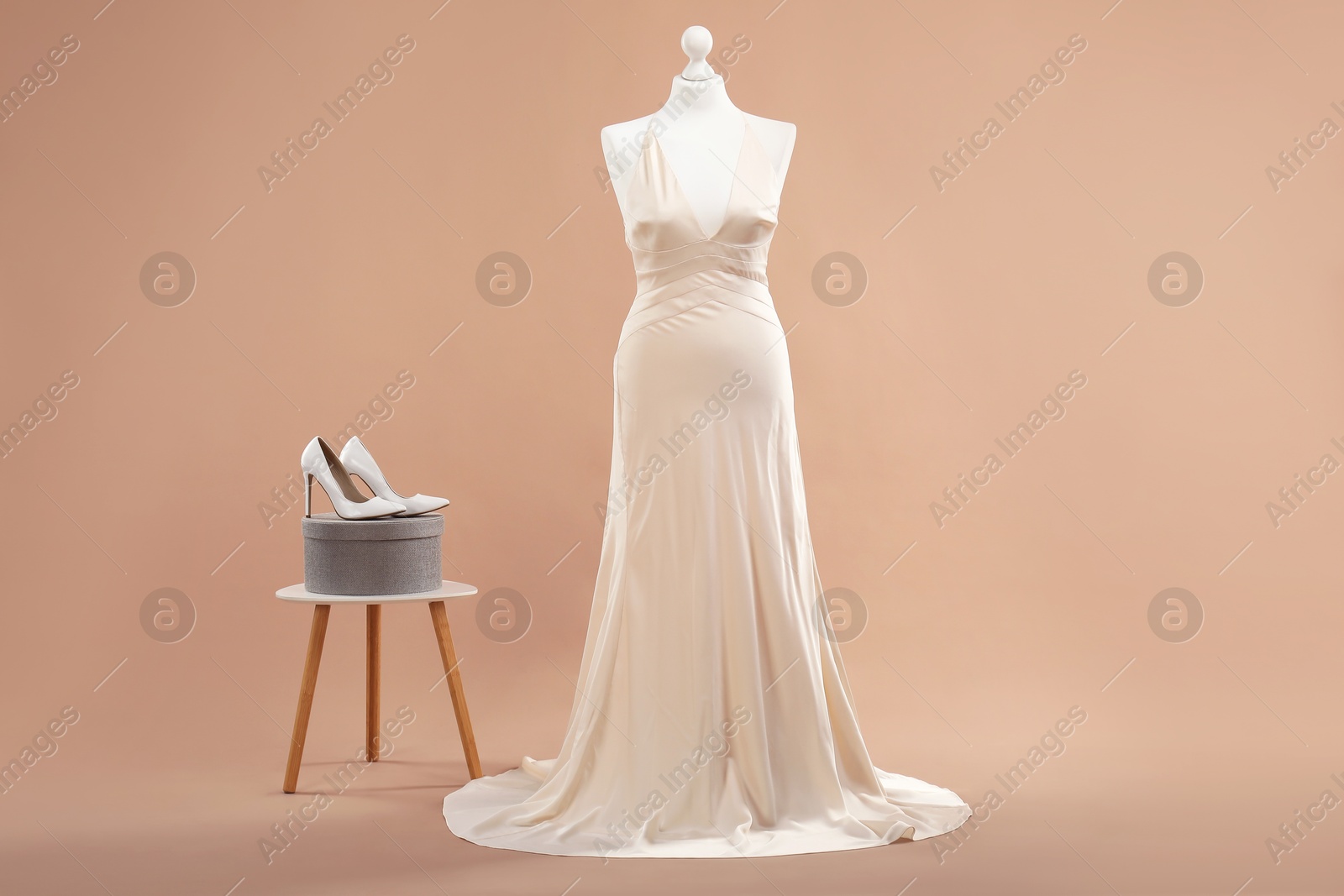 Photo of Mannequin with beautiful wedding dress and shoes on pale brown background