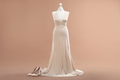 Photo of Mannequin with beautiful wedding dress and shoes on pale brown background