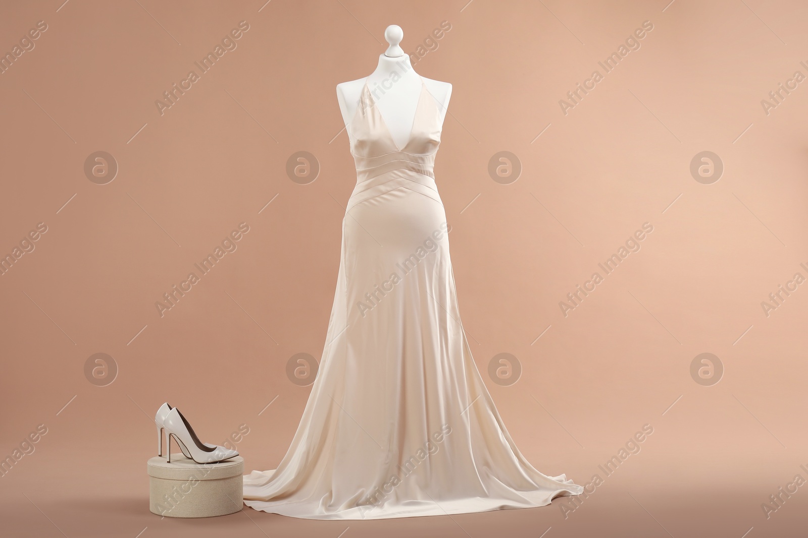 Photo of Mannequin with beautiful wedding dress and shoes on pale brown background