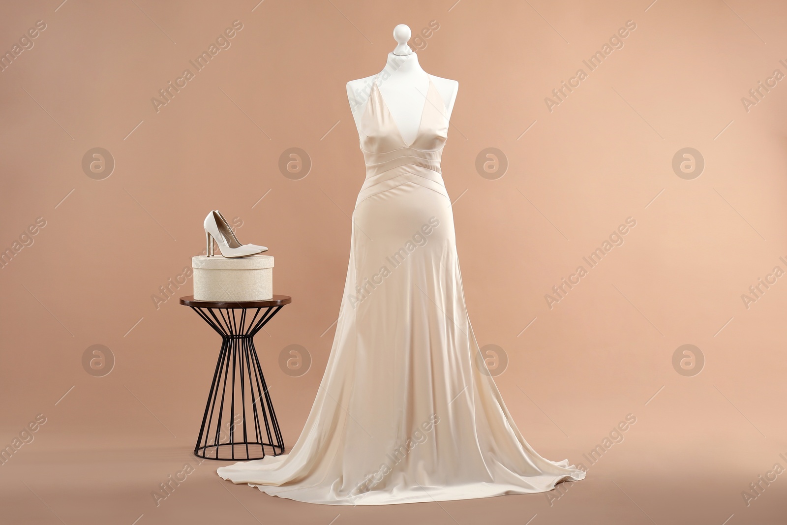 Photo of Mannequin with beautiful wedding dress and shoes on pale brown background