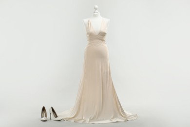 Photo of Mannequin with beautiful wedding dress and shoes on light grey background