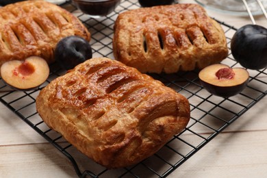 Photo of Delicious puff pastries and plums on white wooden table, closeup