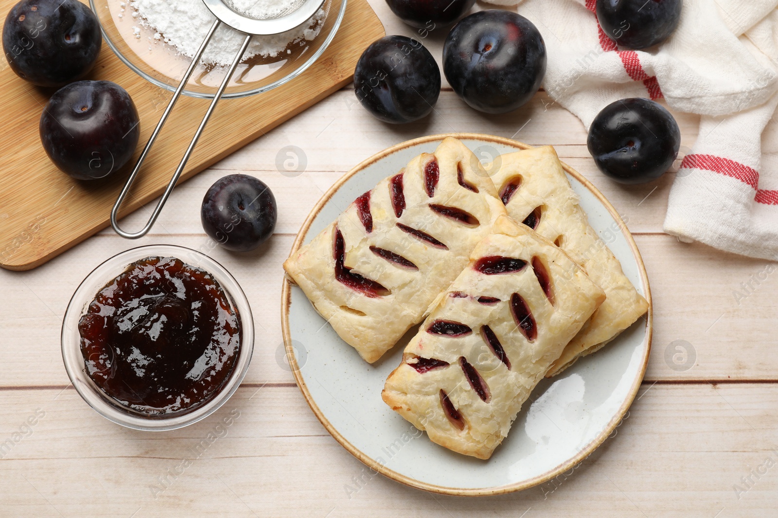 Photo of Delicious puff pastries and plums on white wooden table, flat lay