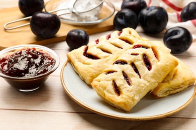 Photo of Delicious puff pastries and plums on white wooden table, closeup