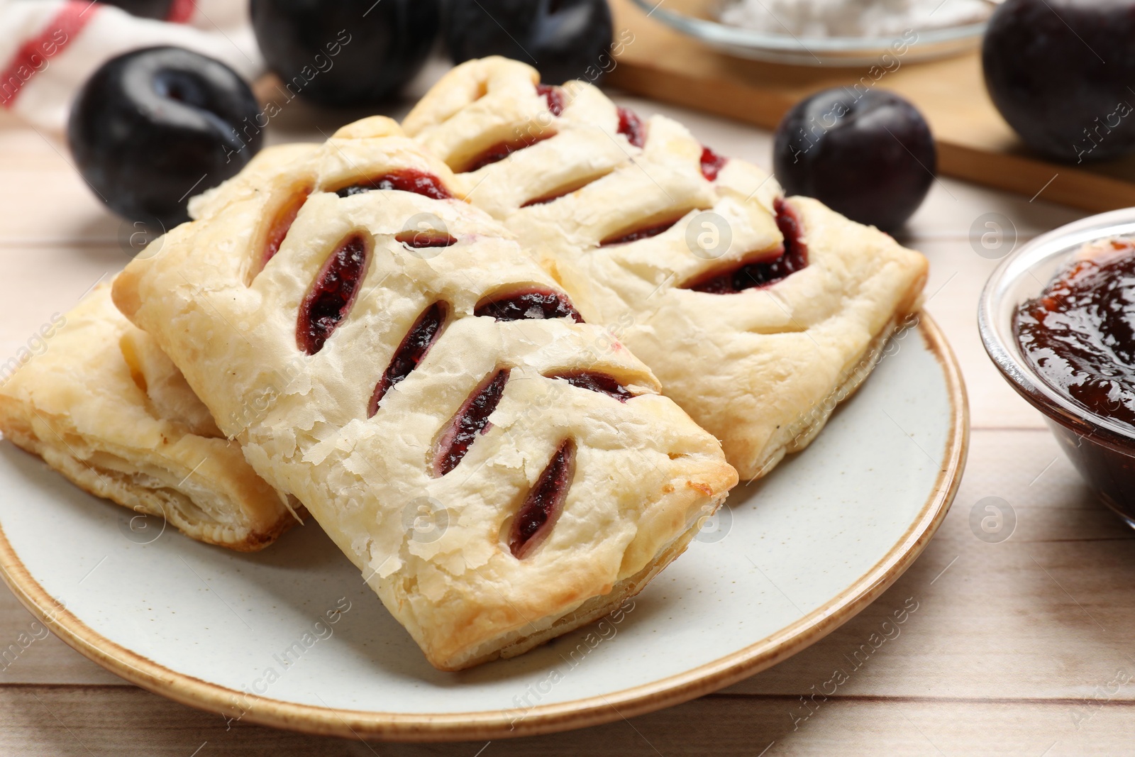 Photo of Delicious puff pastries and plums on white wooden table, closeup