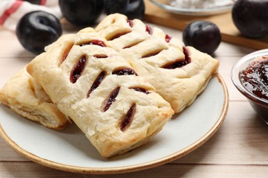 Photo of Delicious puff pastries and plums on white wooden table, closeup