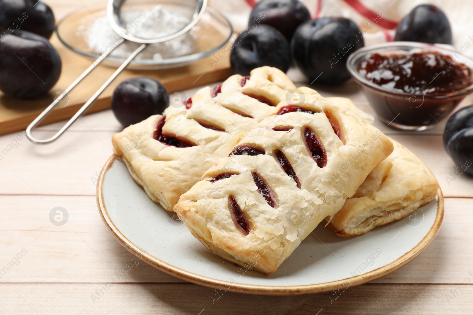 Photo of Delicious puff pastries and plums on white wooden table, closeup