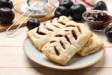 Photo of Delicious puff pastries and plums on white wooden table, closeup