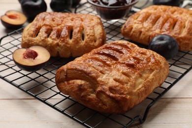 Photo of Delicious puff pastries and plums on white wooden table, closeup