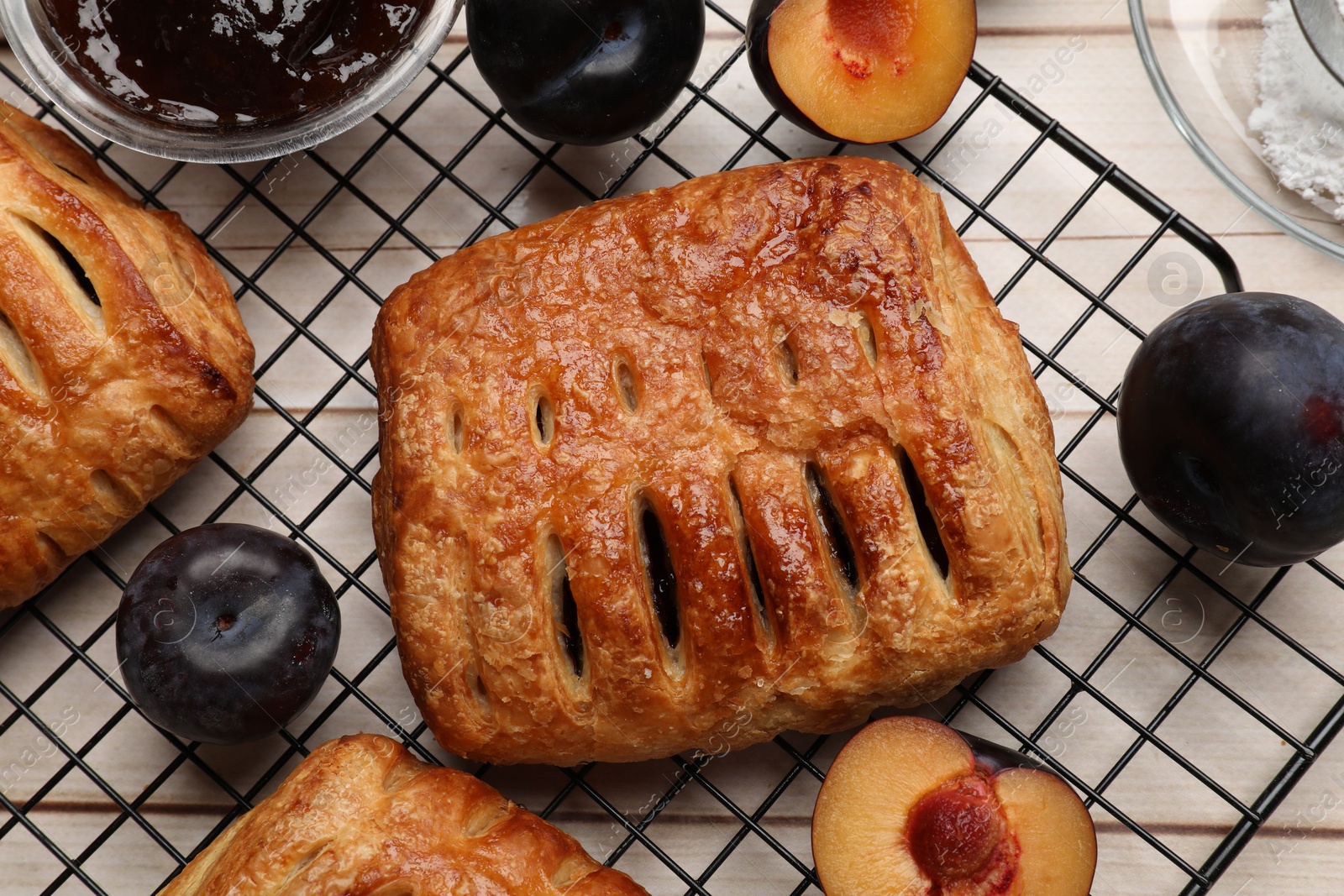 Photo of Delicious puff pastries and plums on white wooden table, flat lay