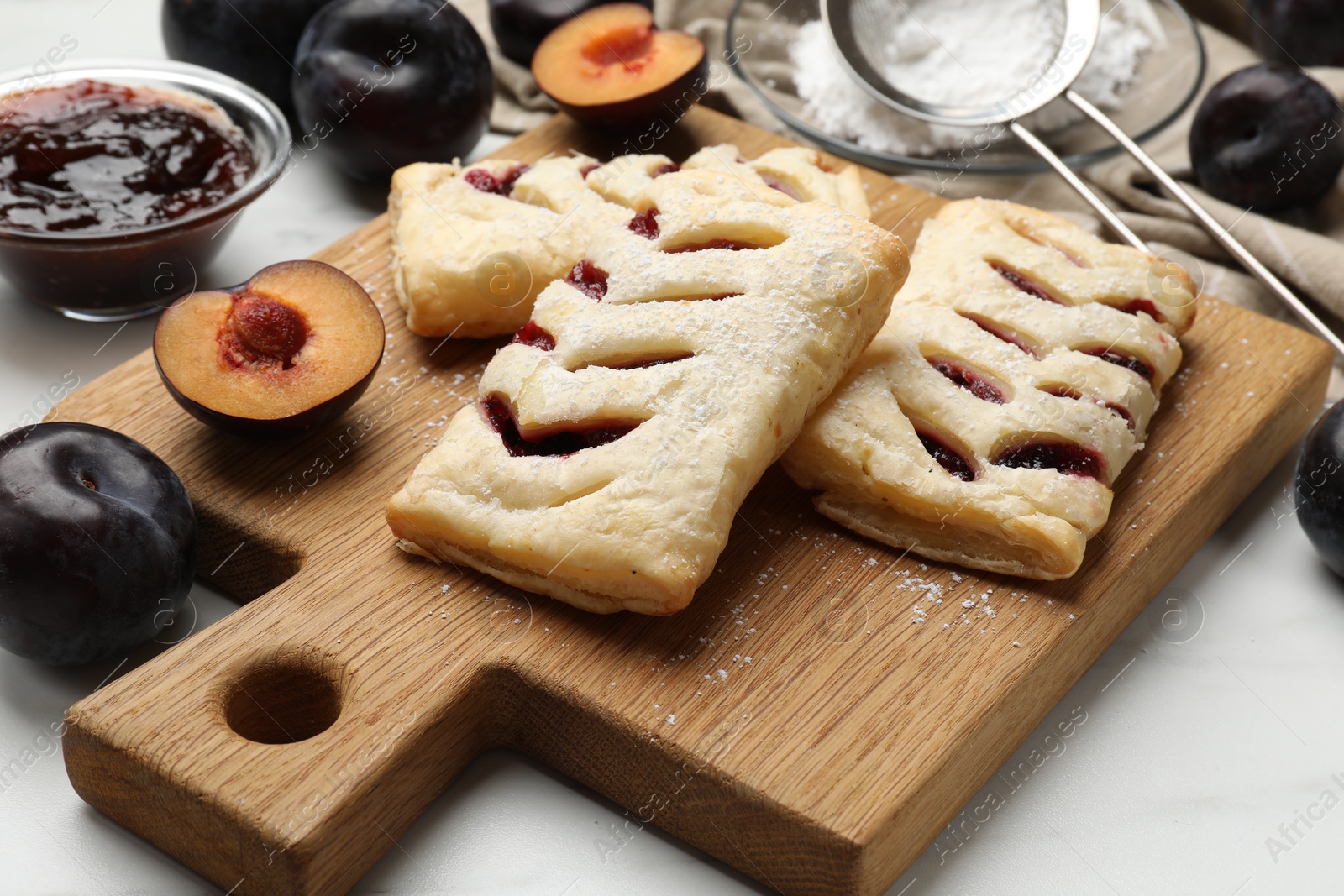 Photo of Delicious puff pastries and plums on white wooden table, closeup