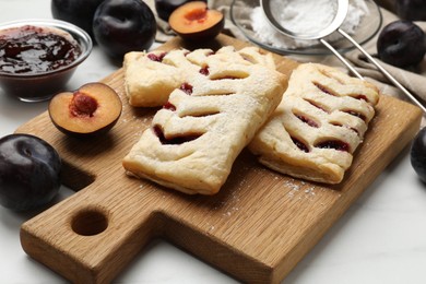 Delicious puff pastries and plums on white wooden table, closeup