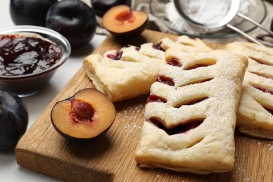 Delicious puff pastries and plums on white wooden table, closeup