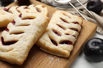 Delicious puff pastries and plums on white wooden table, closeup