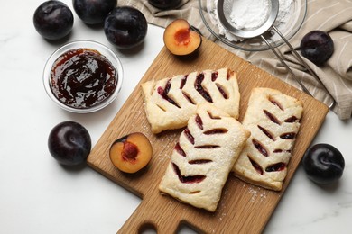 Delicious puff pastries and plums on white wooden table, flat lay