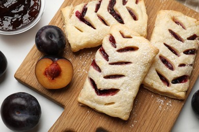 Photo of Delicious puff pastries and plums on white wooden table, flat lay