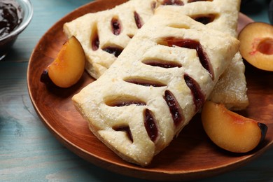 Photo of Delicious puff pastries and plums on light blue wooden table, closeup