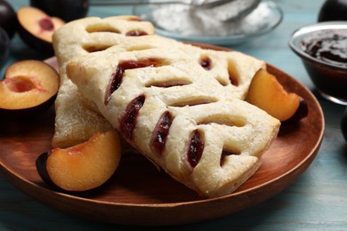 Photo of Delicious puff pastries and plums on light blue wooden table, closeup