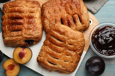 Photo of Delicious puff pastries, jam and plums on light blue wooden table, top view