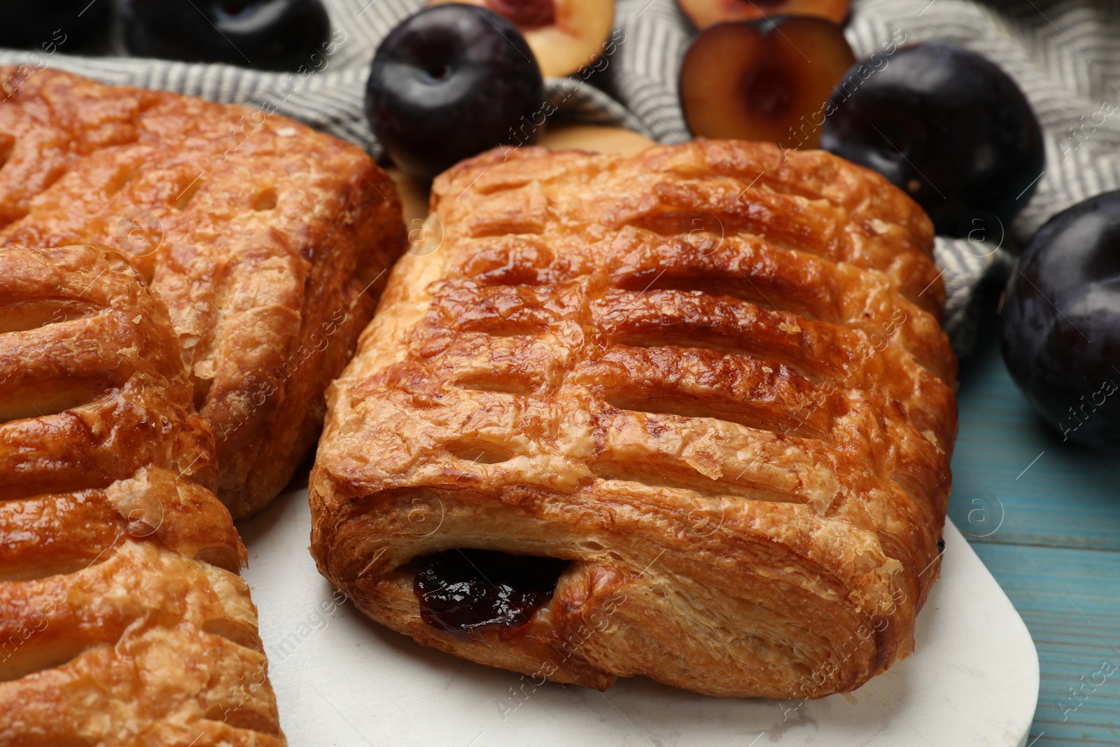 Photo of Delicious puff pastries and plums on light blue wooden table, closeup