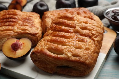 Photo of Delicious puff pastries and plums on light blue wooden table, closeup