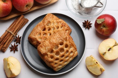 Photo of Delicious puff pastries, apples, cinnamon, anise stars and powdered sugar on white tiled table, top view