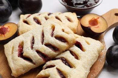 Delicious puff pastries and plums on table, closeup