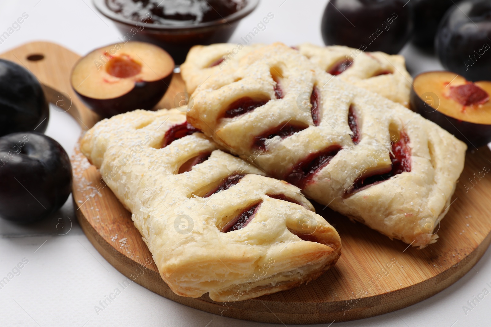 Photo of Delicious puff pastries and plums on white table, closeup