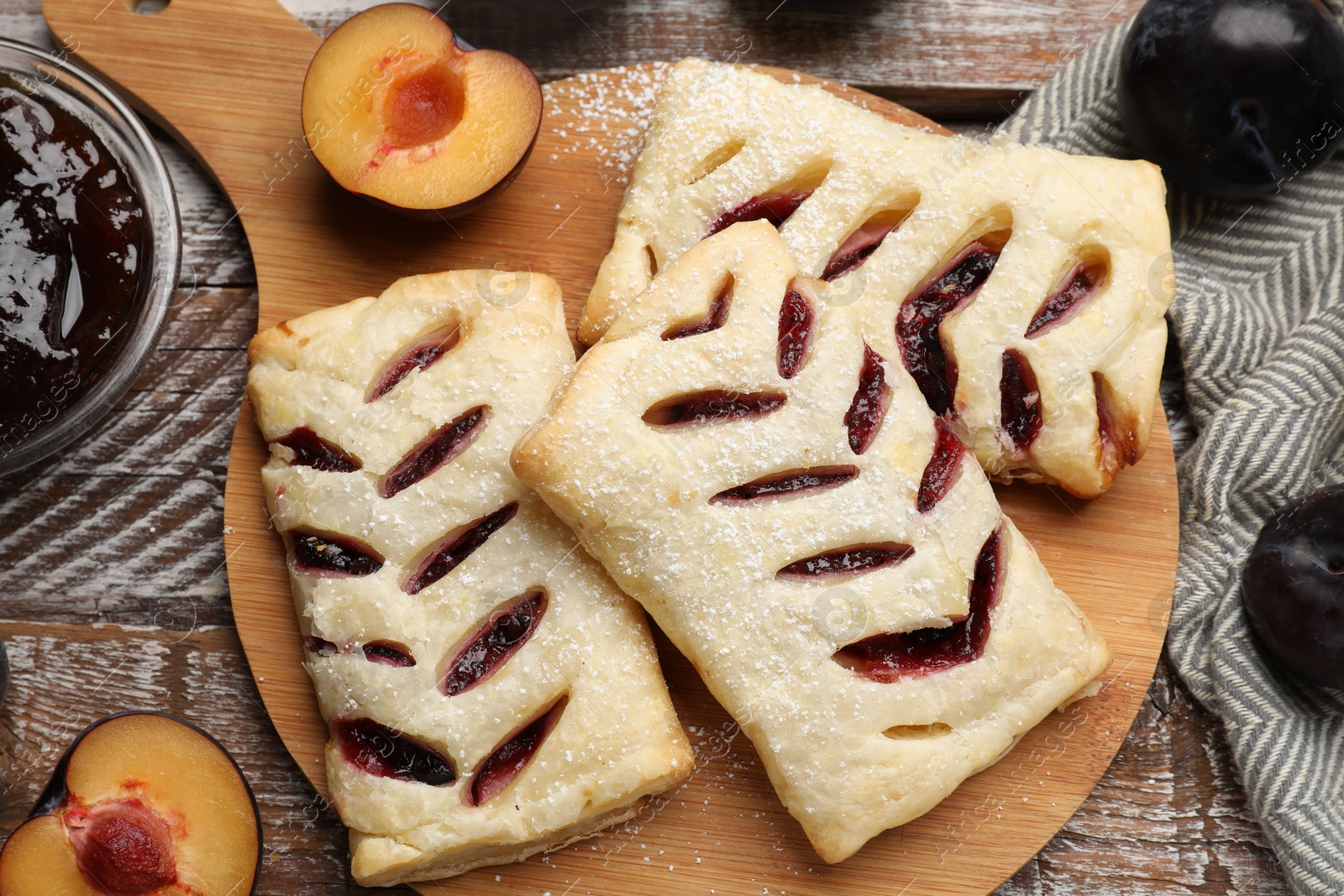 Photo of Delicious puff pastries, plums and jam on wooden table, top view