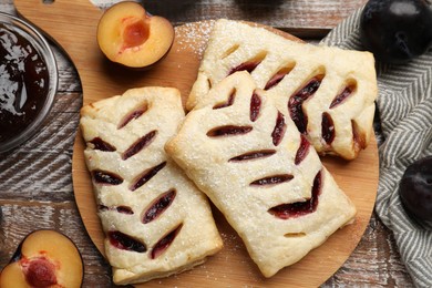 Delicious puff pastries, plums and jam on wooden table, top view