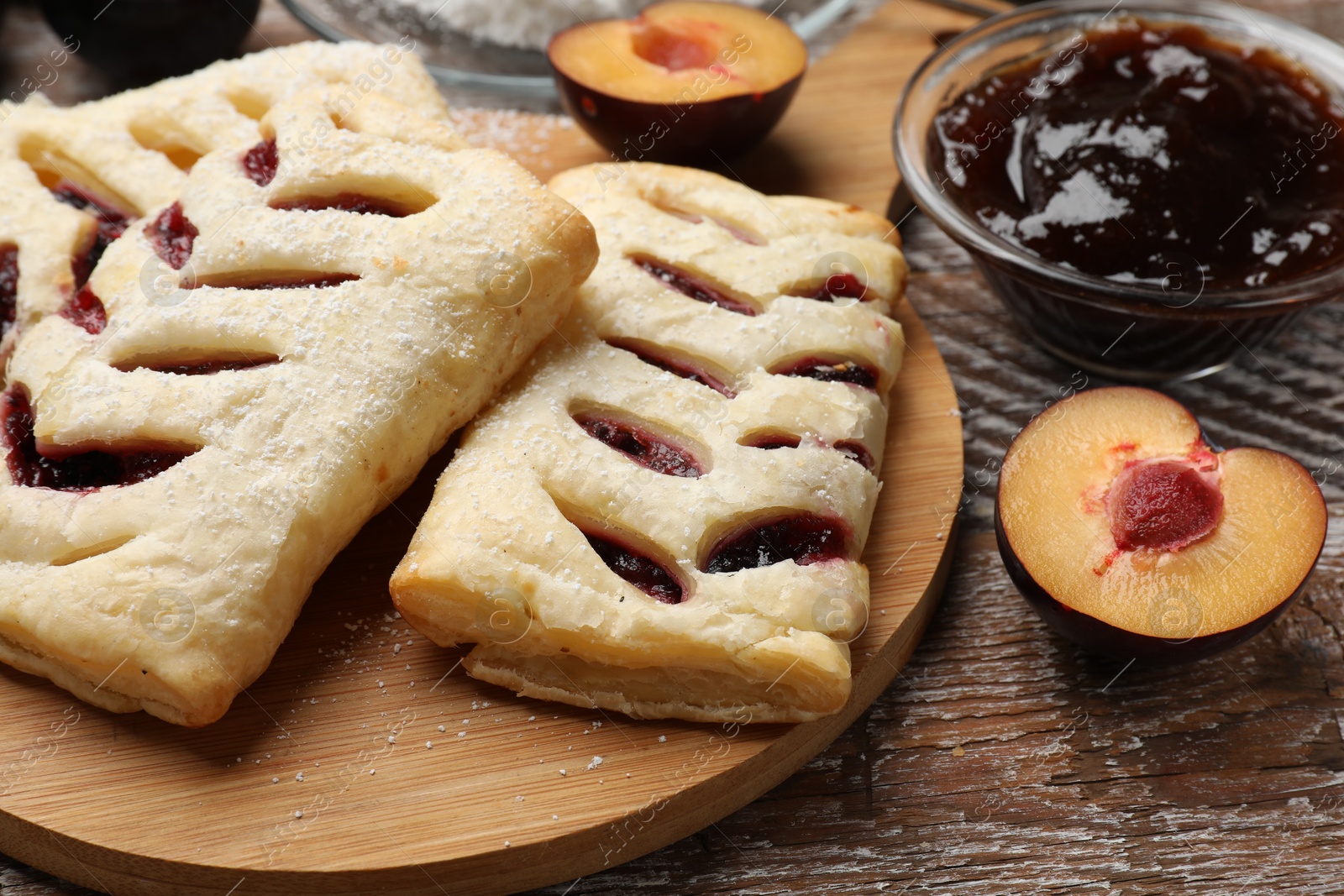 Photo of Delicious puff pastries, plums and jam on wooden table, closeup