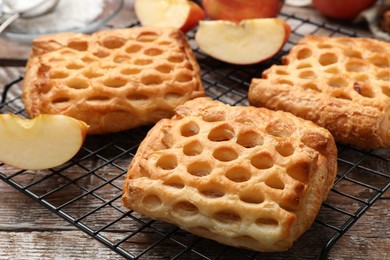 Photo of Delicious puff pastries with fruit filling and apples on wooden table, closeup