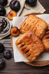 Delicious puff pastries, jam and plums on wooden table, top view