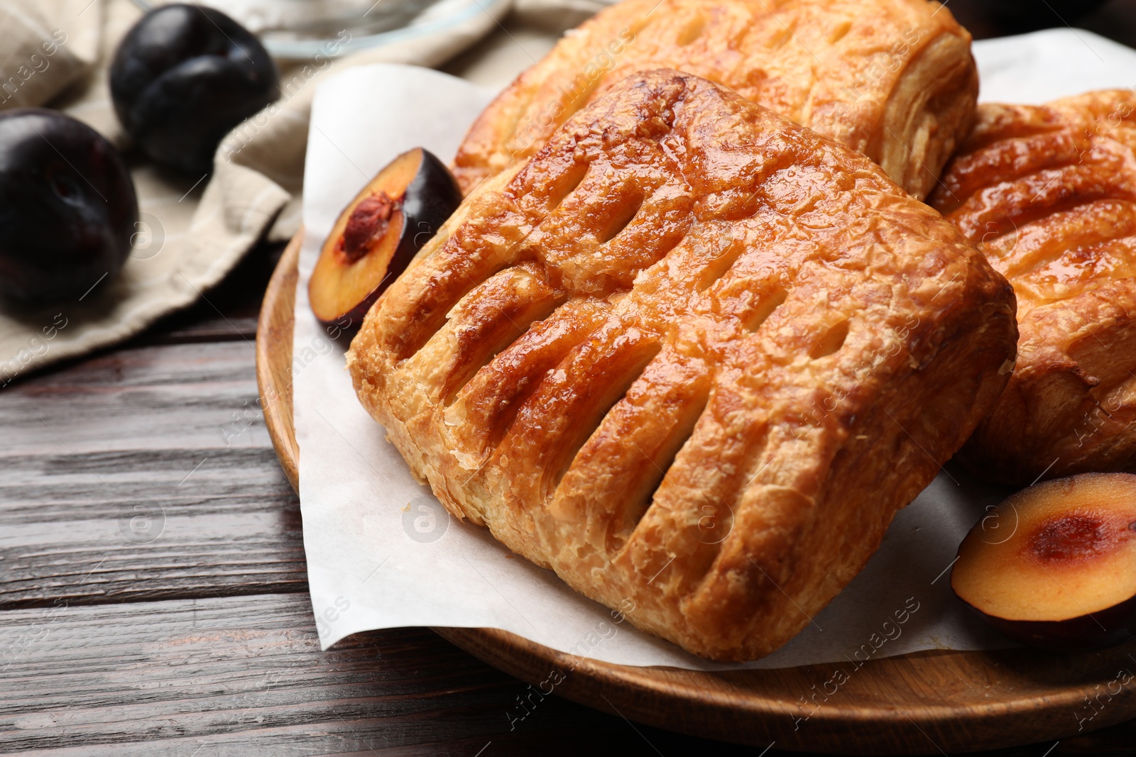 Photo of Delicious puff pastries and plums on wooden table, closeup