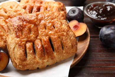 Photo of Delicious puff pastries, jam and plums on wooden table, closeup