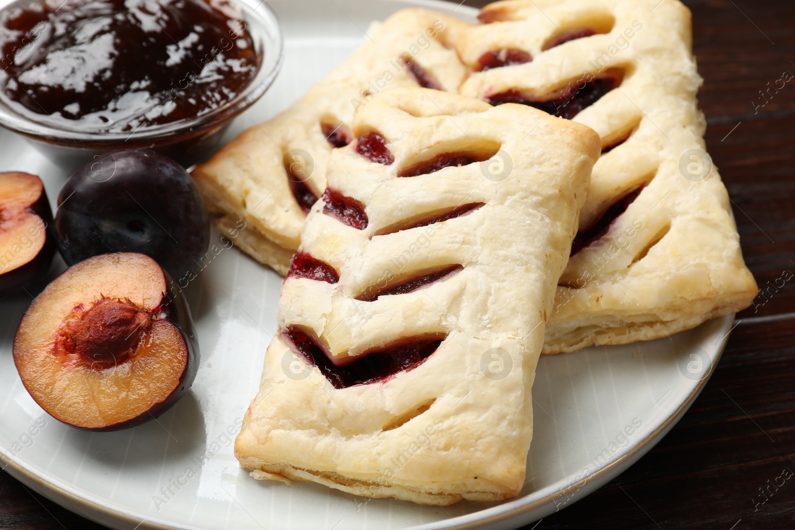 Photo of Delicious puff pastries, jam and plums on table, closeup