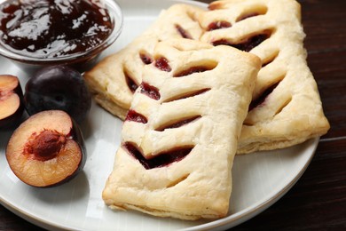 Delicious puff pastries, jam and plums on table, closeup