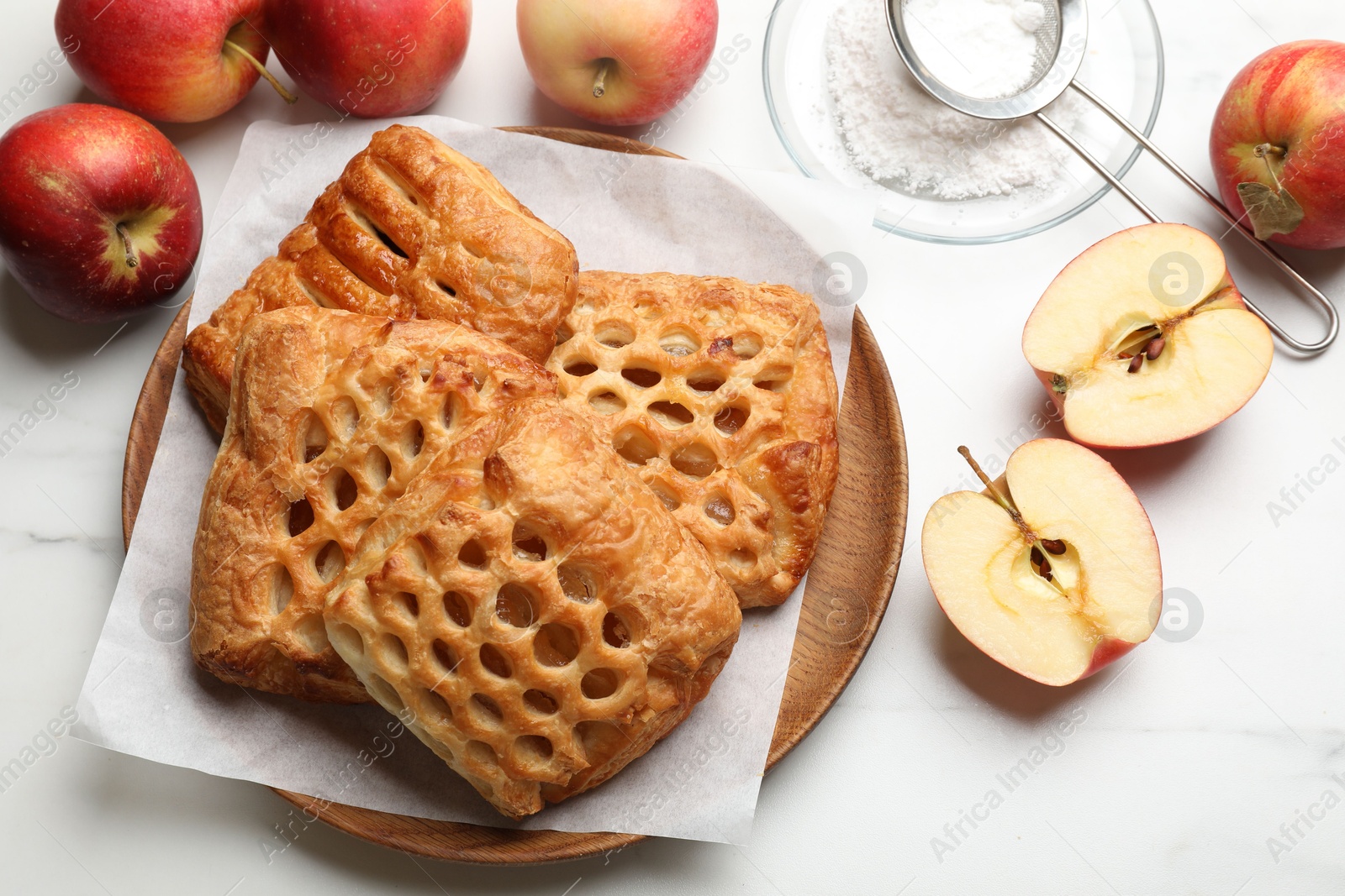 Photo of Delicious puff pastries, apples and powdered sugar on white marble table, top view