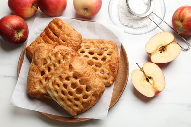 Photo of Delicious puff pastries, apples and powdered sugar on white marble table, top view