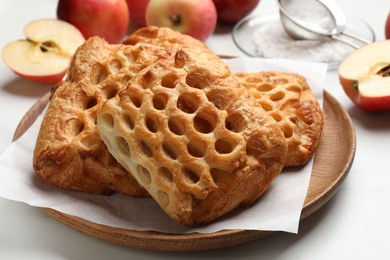 Photo of Delicious puff pastries, apples and powdered sugar on white table, closeup