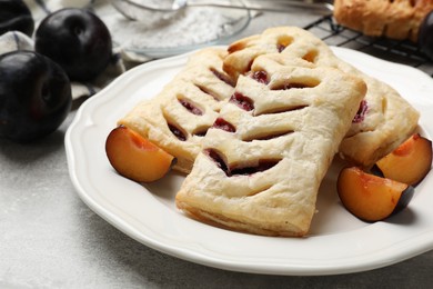 Photo of Delicious puff pastries and plums on grey table, closeup