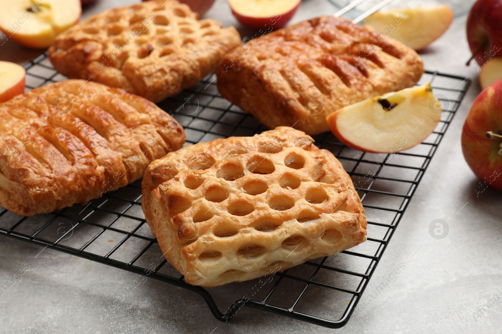 Photo of Delicious puff pastries with fruit filling and apples on grey table, closeup