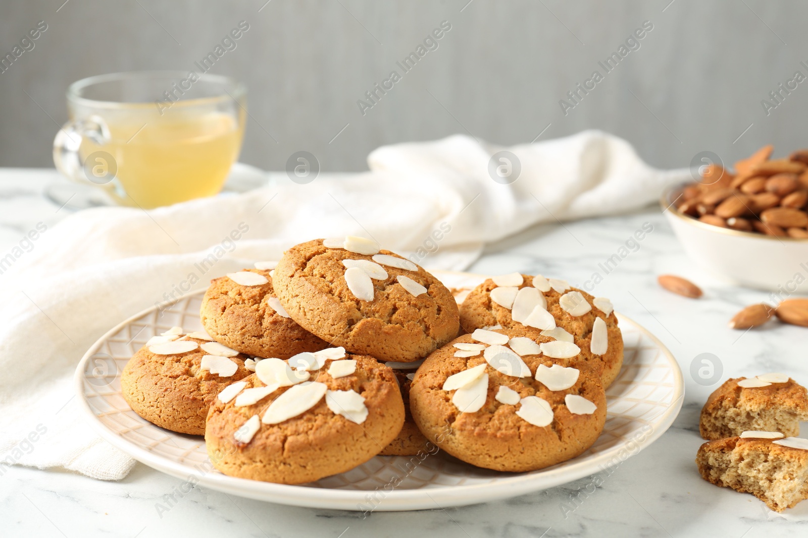 Photo of Tasty cookies with almond flakes, nuts and tea on white marble table, closeup