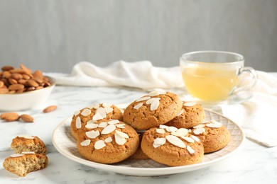 Photo of Tasty cookies with almond flakes, nuts and tea on white marble table, closeup