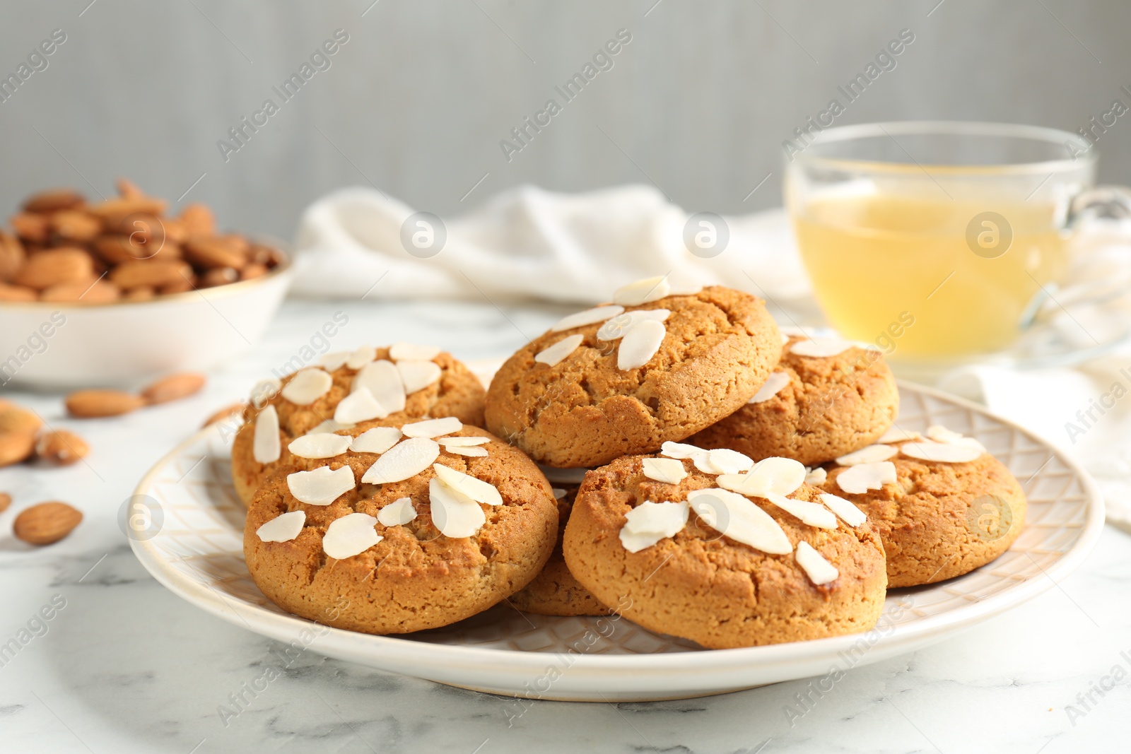 Photo of Tasty cookies with almond flakes, nuts and tea on white marble table, closeup