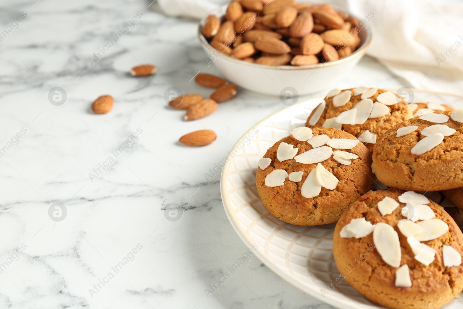 Photo of Tasty cookies with almond flakes and nuts on white marble table, closeup. Space for text