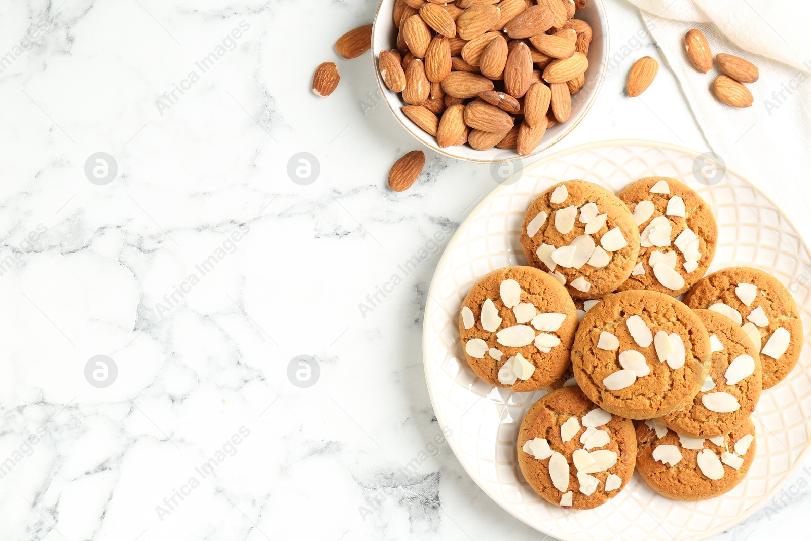 Photo of Tasty cookies with almond flakes and nuts on white marble table, top view. Space for text