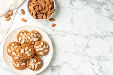 Photo of Tasty cookies with almond flakes and nuts on white marble table, top view. Space for text